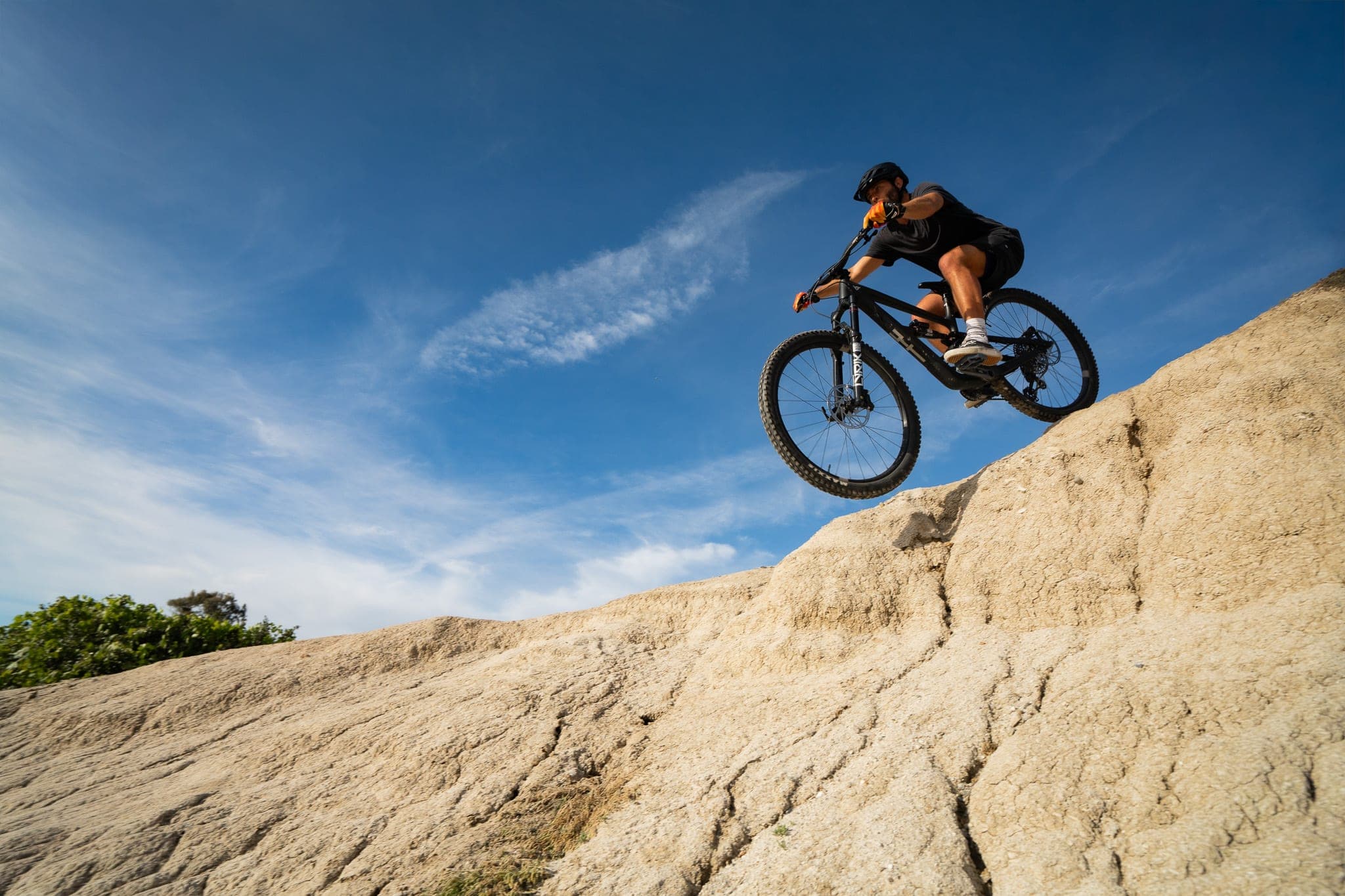 Mountain biker dropping down a sandstone ridge against a bright blue sky