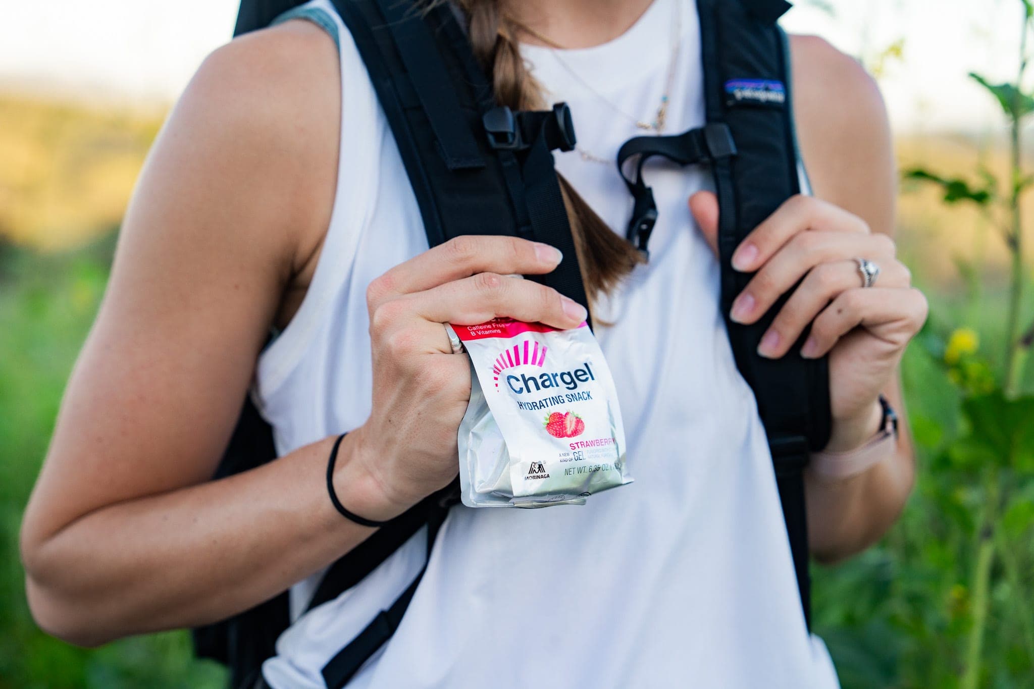 Close-up of a hiker with a backpack holding a strawberry Chargel gel pouch on a sunny trail