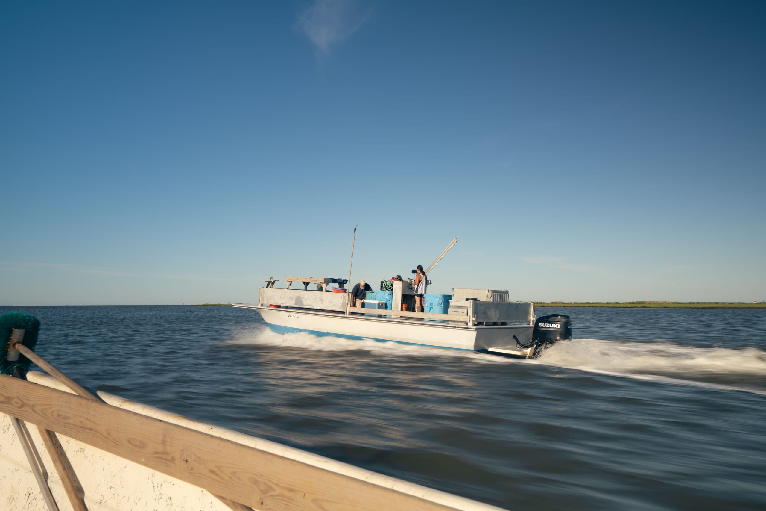 Oyster workboat skimming across a calm bay under a clear blue sky, seen from a neighboring boat