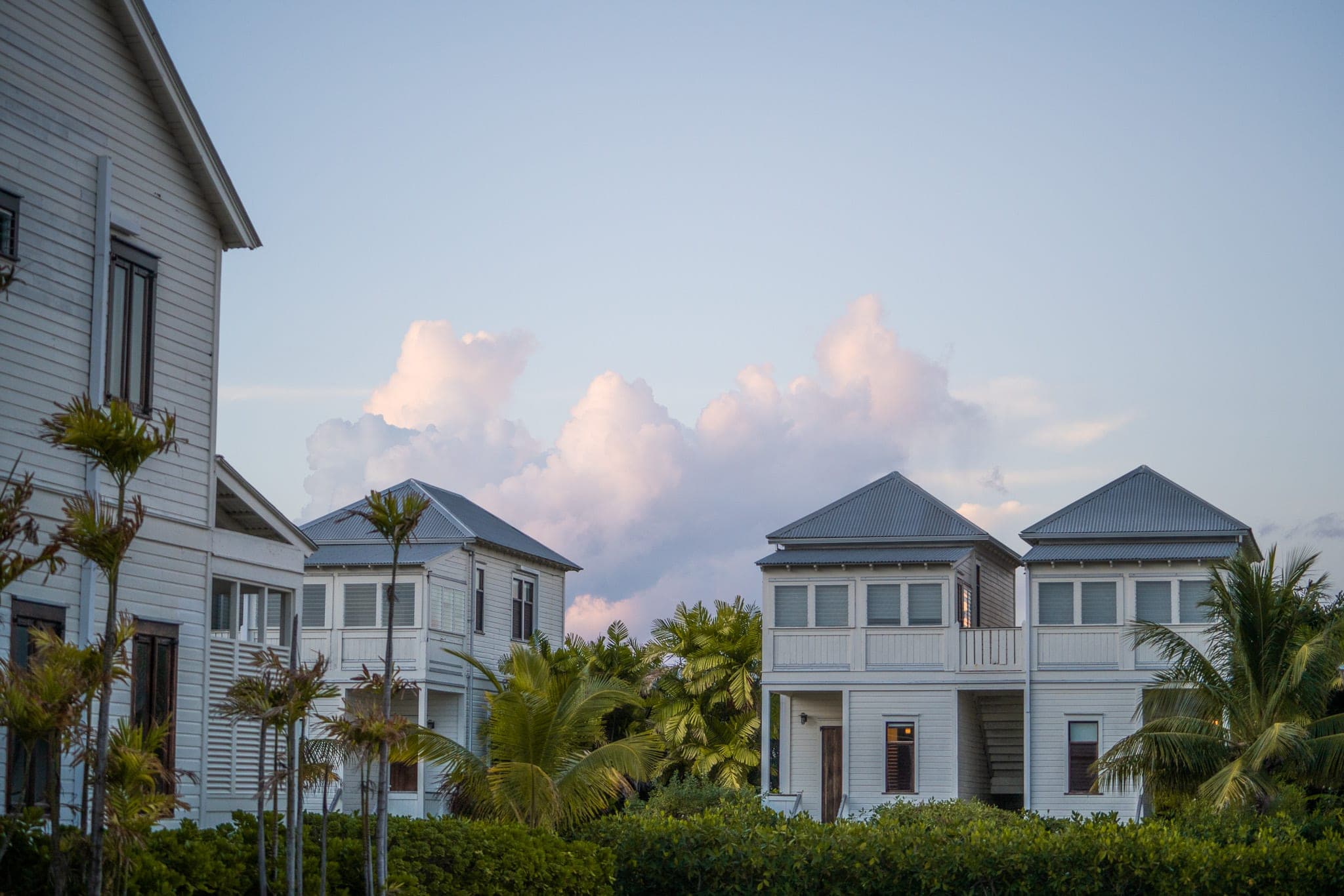 White coastal cottages with metal roofs tucked among palms beneath a pastel evening sky