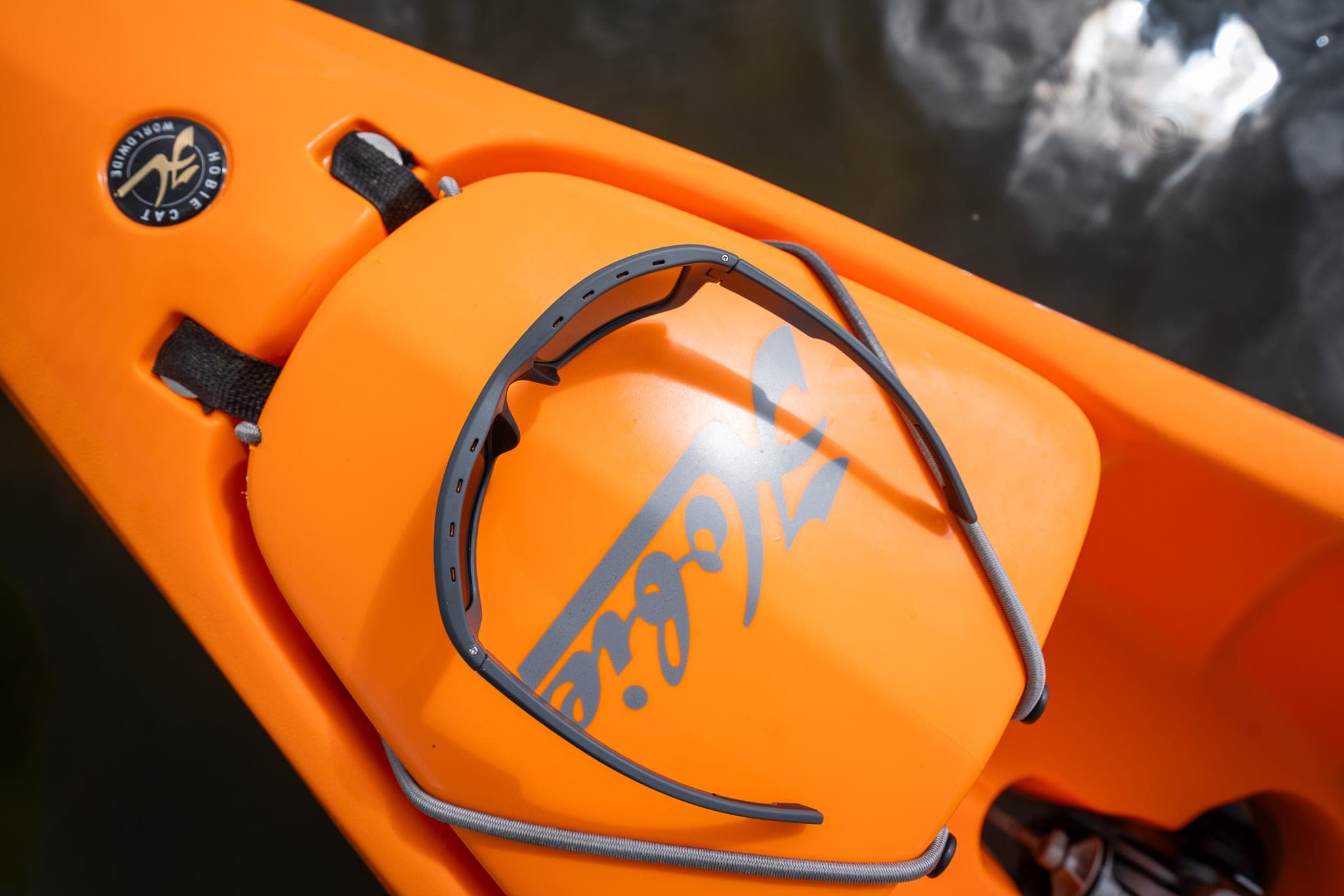 Sunglasses resting on the bow of an orange Hobie kayak floating over dark water