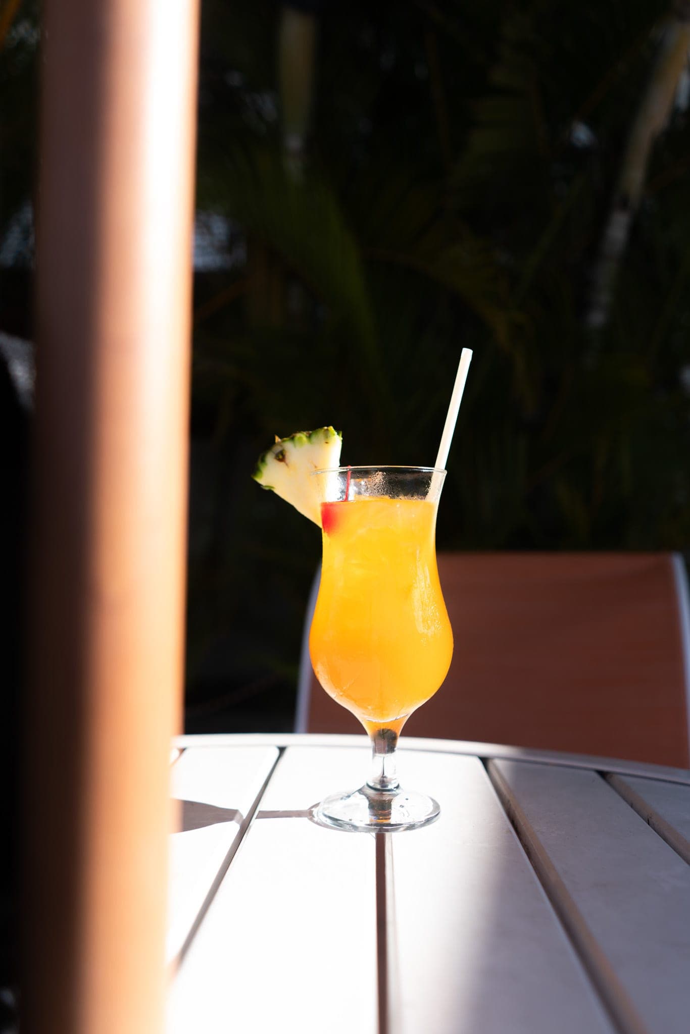 Tropical cocktail with pineapple garnish glowing in a shaft of sunlight on a patio table