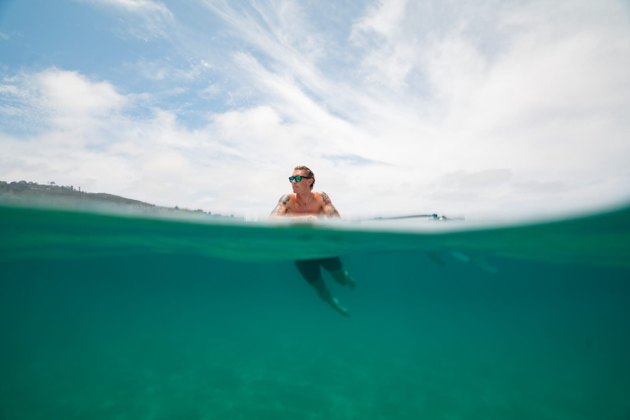 Split over-under view of a surfer sitting on his board in glassy turquoise water