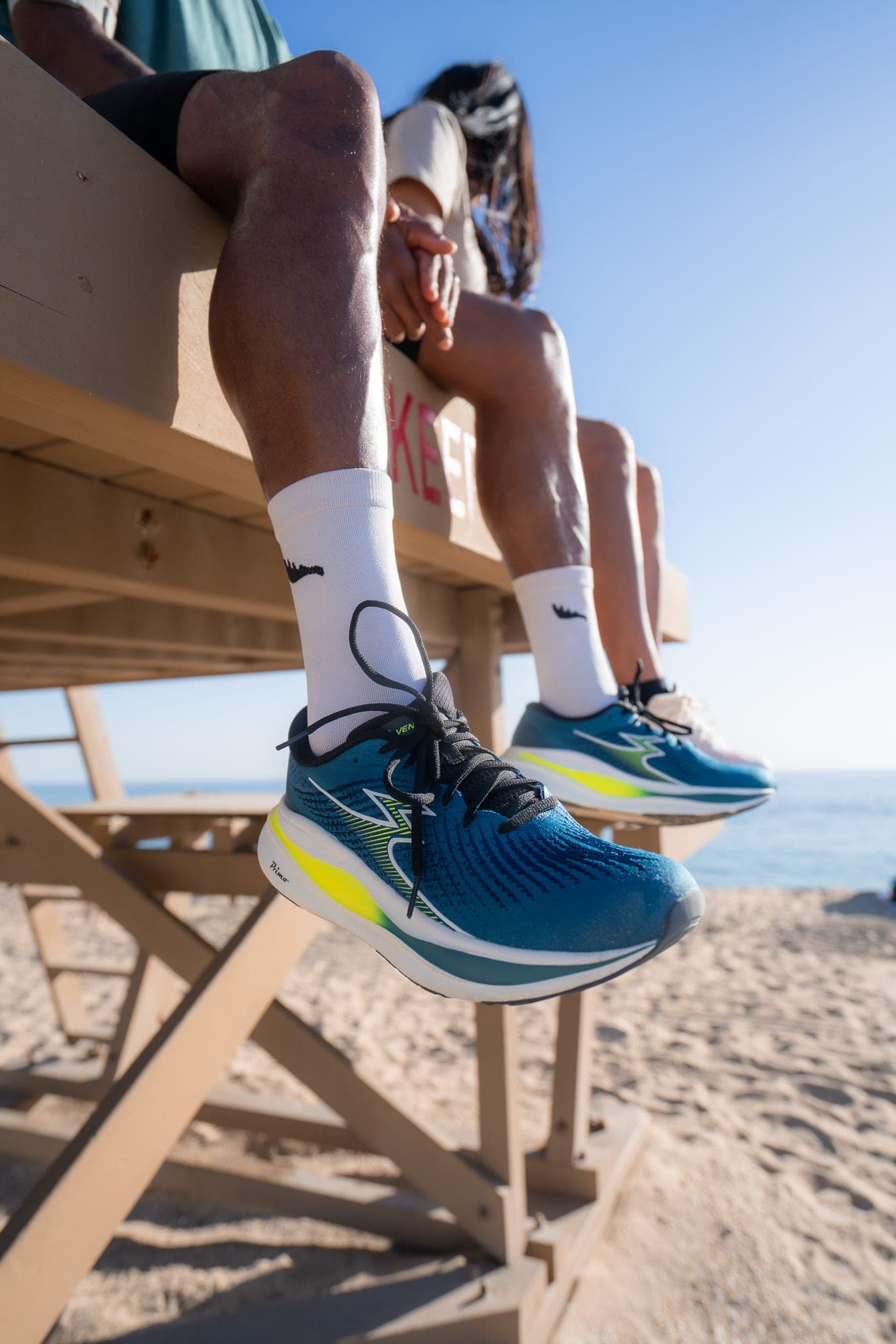 Close-up of runners' shoes dangling from a wooden lifeguard tower on a sunny beach
