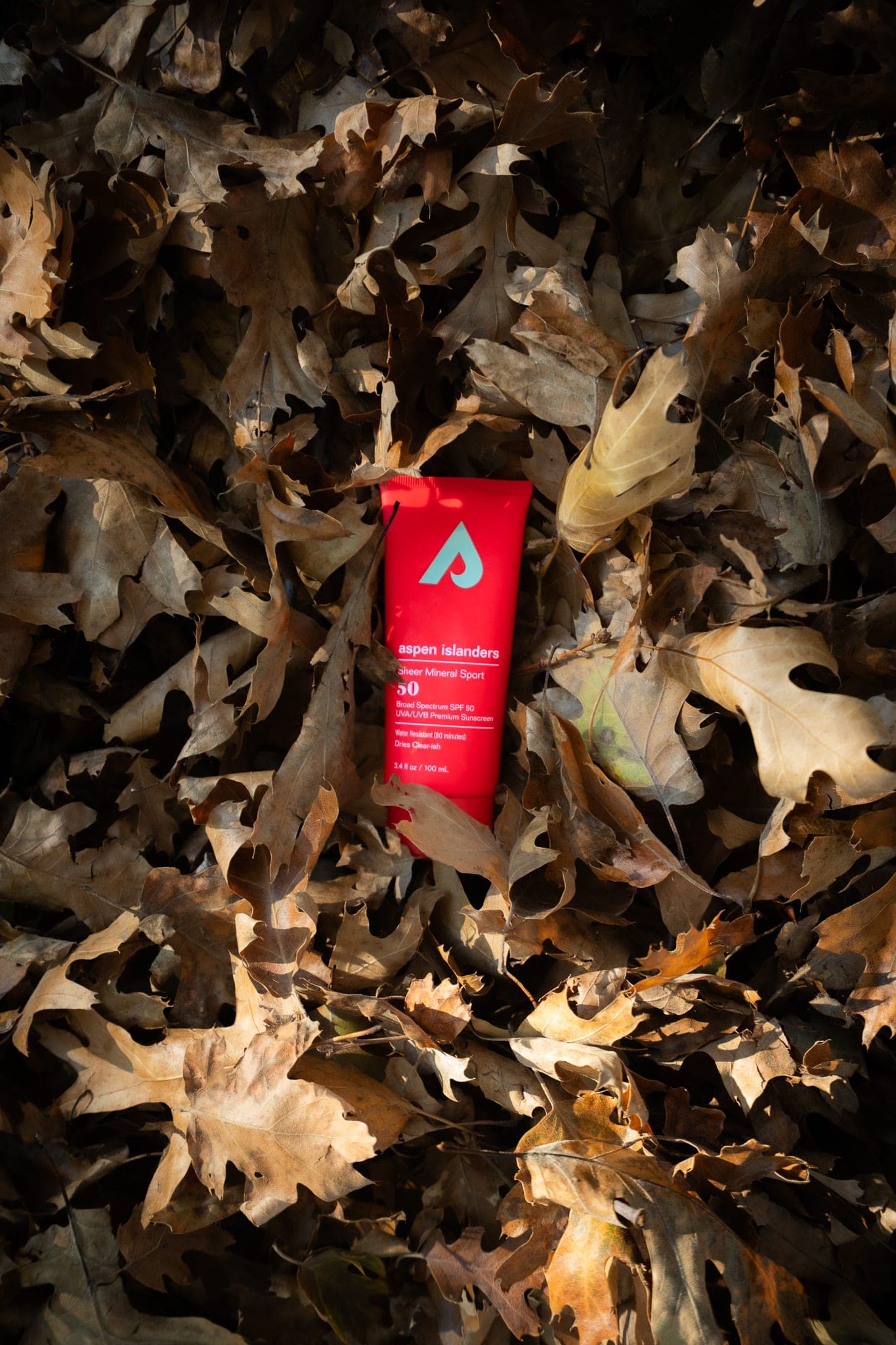 Red tube of mineral sunscreen nestled in a bed of dry autumn oak leaves